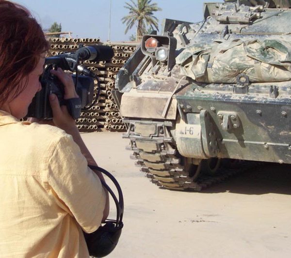 Projekt "Hallo Krieg". Eine Frau steht mit einer Filmkamera vor einem Panzer.
