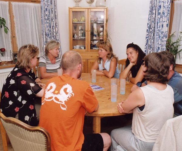 Projekt "ELTERNTALK". An einem runden Tisch sitzen Erwachsene zusammen und unterhalten sich.