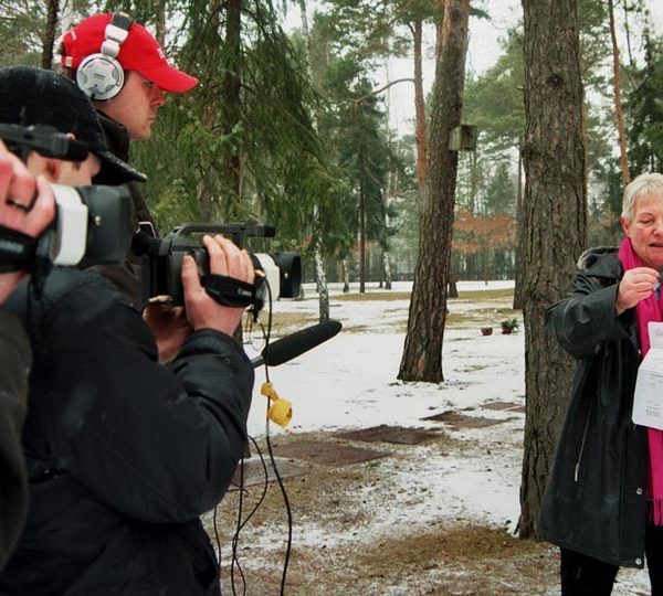 Projekt "Kleines Halbe, große Geschichte". Drei Jugendliche, die mit Tongerät, Kopfhörern und Filmkameras ausgestattet sind, filmen eine ältere Dame vor einer winterlichen Außenkulisse.