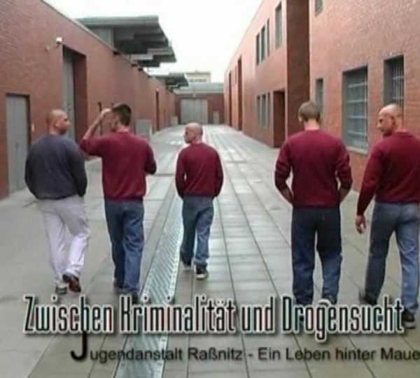 Projekt „Zwischen Kriminalität und Drogensuch – Jugendanstalt Raßnitz ein Leben hinter Mauern". Fünf junge Männer in einheitlicher Kleidung gehen durch einen Innenhof.