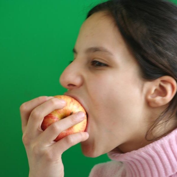 Projekt ""Man ist, was man isst" - eine Tangible Media-Videoinstallation". Großaufnahme des Gesichts eines Mädchens, das vor einem Greenscreen in einen Apfel beißt.