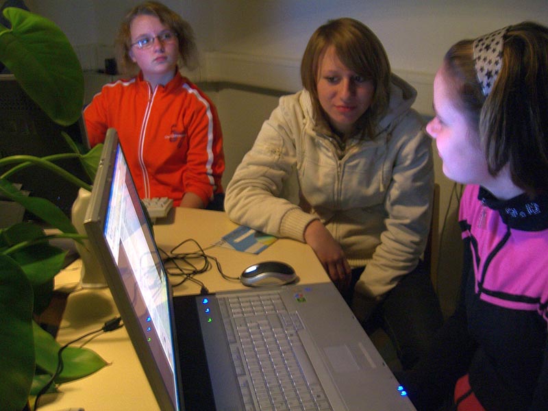 Projekt "Multiline". Drei junge Frauen sitzen gemeinsam an einem Tisch, auf welchem ein Laptop steht.