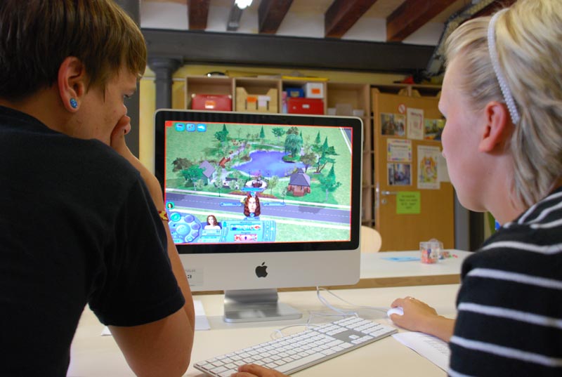 Projekt ""Trapped" - Auseinandersetzung mit Gefahren durch das Internet". Aufnahme von zwei Jugendlichen, die vor einem Computerbildschirm sitzen und "die Sims" spielen.