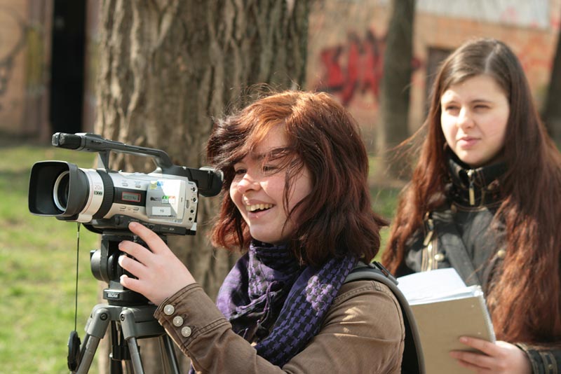 Projekt "Lebensläufe - Dokumentarfilmprojekt & Bukowina Style - Eine filmische Spurensuche". Ein Mädchen steht hinter einer Filmkamera. Dahinter steht ein weiteres und hält einen Block in der Hand.
