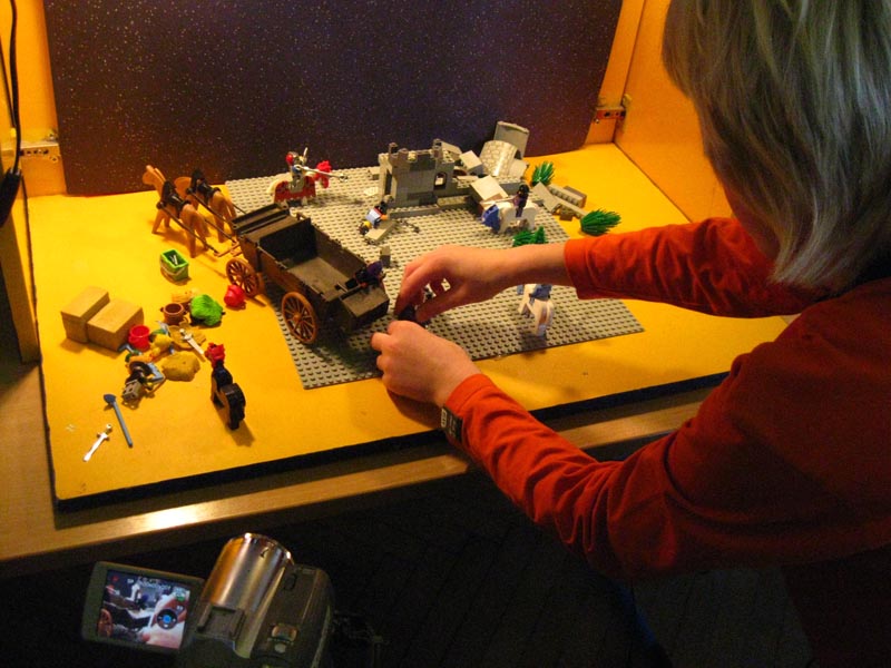 Projekt "Offener Kanal Merseburg-Querfurt". Ein Kind verändert eine mit Lego und Playmobil aufgebaute Kulisse. Neben dem Kind steht eine Videokamera.