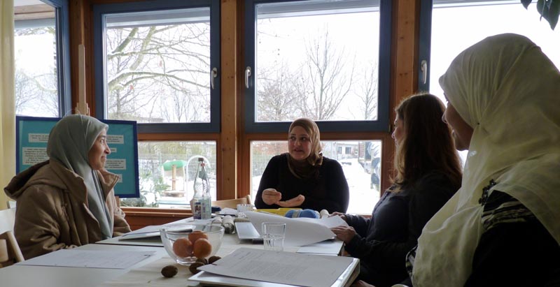 Projekt "MedienFit - SprachFit". Vier Frauen sitzen gemeinsam um einen Tisch und unterhalten sich. Auf dem Tisch liegen Unterlagen.