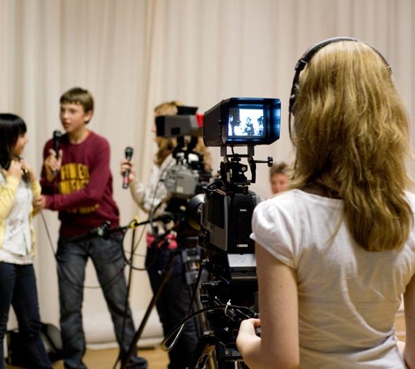 Projekt "Schulversuch "Schulische Medienbildung in Mecklenburg-Vorpommern"". Eine Jugendliche filmt mit einer Filmkamera vier weitere Jugendliche. Zwei von ihnen halten Mikrofone in der Hand.