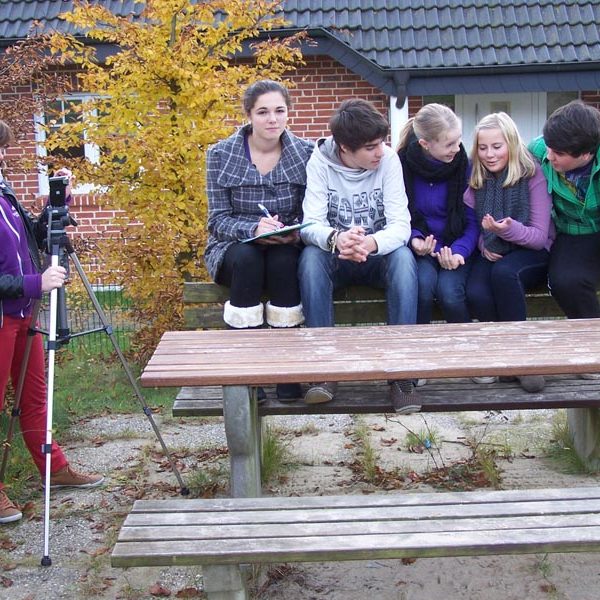 Projekt "Jäger des Vergessenen". Fünf Jugendliche sitzen auf der Lehne einer Bank, eine weitere steht mit einer Kamera daneben und filmt sie.