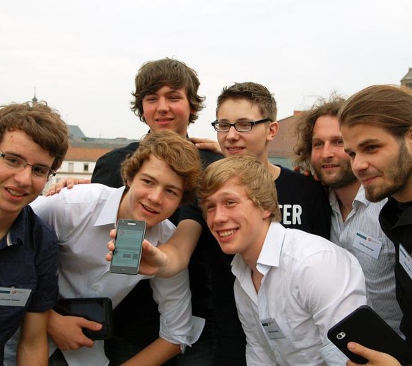 Projekt "Kaiserdom-App - App durch die Stadt!". Gruppenfoto mit sieben jungen Männern. Einer von ihnen hält ein Smartphone in die Kamera.