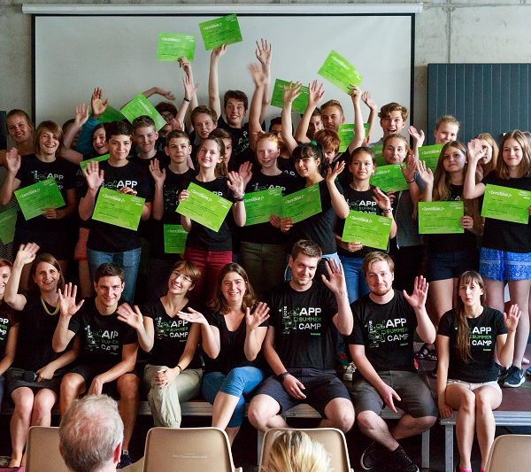 #Projekt "App Summer Camp". Gruppenfoto der Teilnehmenden. Sie stehen und sitzen auf einer Bühne und tragen das gleiche T-Shirt.
