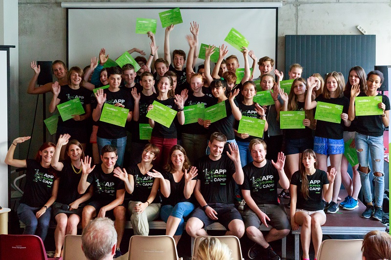 #Projekt "App Summer Camp". Gruppenfoto der Teilnehmenden. Sie stehen und sitzen auf einer Bühne und tragen das gleiche T-Shirt.