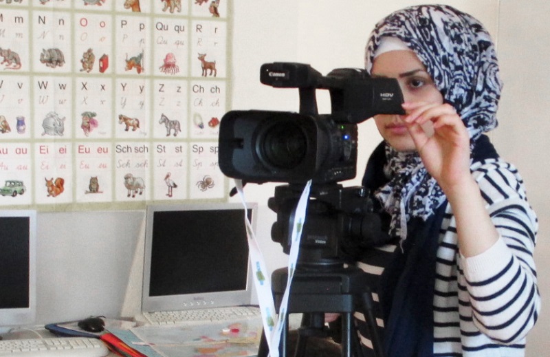 Foto einer jungen Frau, die hinter einer Filmkamera steht.