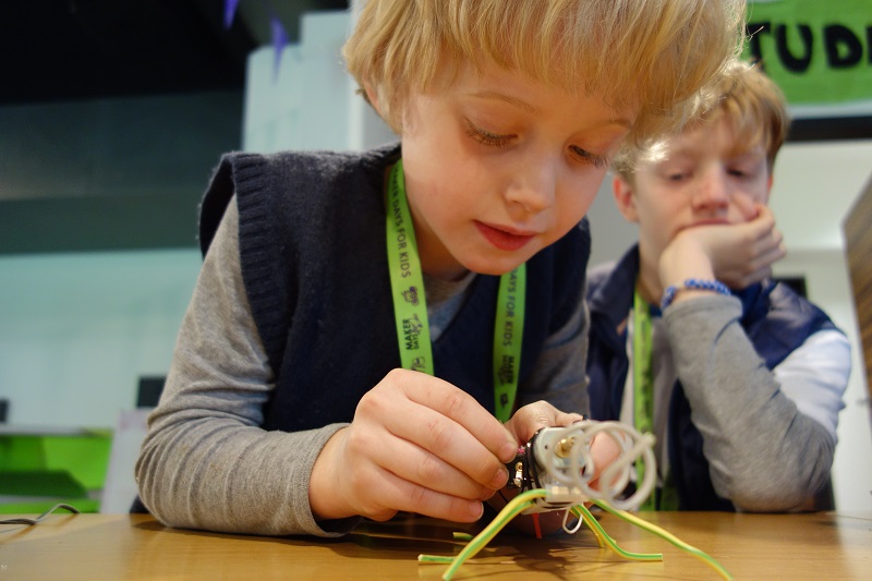 Projekt "Maker Days for kids". Zwei Jungen sitzen an einem Tisch, einer von ihnen hält ein Gerät in der Hand und betrachtet es.