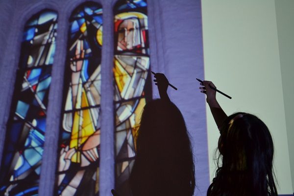 Projekt "Das Medienatelier - Digitale Medien als eine von 100 Sprachen". An eine Wand wird das Bild von Kirchenfenstern projiziert. Davor steht ein Mädchen mit einem Stift in der Hand.