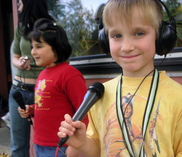 Foto von zwei Kindern, die mit Mikrofonen und Kopfhörern ausgestattet sind.