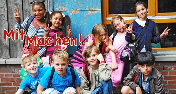 Gruppenfoto von neun Kindern, die vor einer Hauswand posieren. Beschriftet ist das Bild mit den Worten "Mit Machen!".