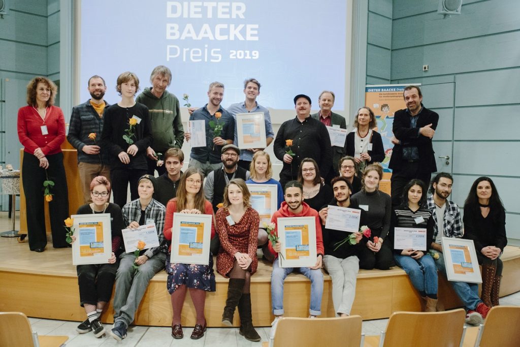 Gruppenfoto der Preisträger und Preisträgerinnen des Dieter Baacke Preises 2021. Sie sitzen und stehen auf dem Podium und halten ihre Urkunden in den Händen.