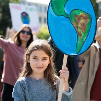 Foto eines Mädchens, das bei einer Demonstration ein Schild in Form der Erdkugel hält.