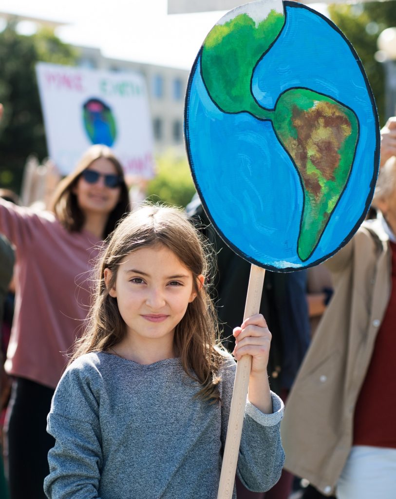 Foto eines Mädchens, das bei einer Demonstration ein Schild in Form der Erdkugel hält.