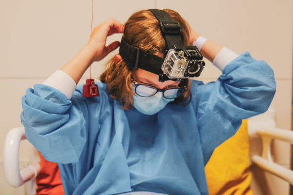 Foto von der Entstehung einer Videosequenz für das Projekt "Who am I". Das abgebildete Kind sitzt auf einem Krankenbett und trägt einen Action-Camcorder auf dem Kopf.