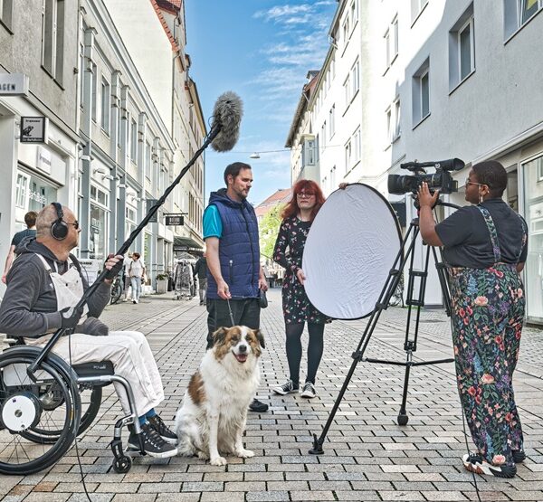 Kamerateam filmt eine Frau und einen Mann mit Hund in Fußgängerzone
