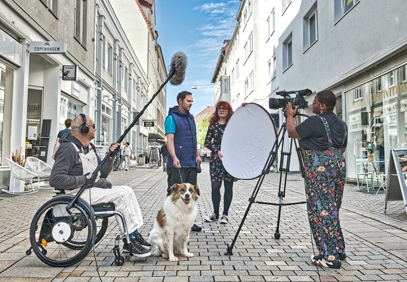 Kamerateam filmt eine Frau und einen Mann mit Hund in Fußgängerzone