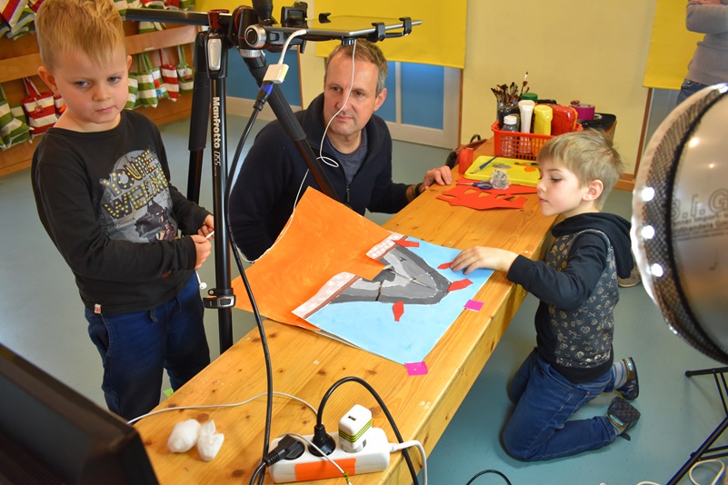 Zwei Kita-Kinder und ein Erzieher fotografieren ein selbstgemaltes Bild