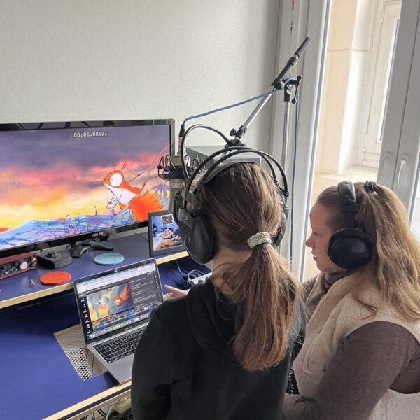 Zwei Jugendliche sitzen nmit Kopfhörern vor einem Laptop und einem Bildschirm